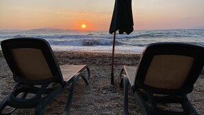 Dos sillas de playa mirando al océano con un atardecer de fondo.