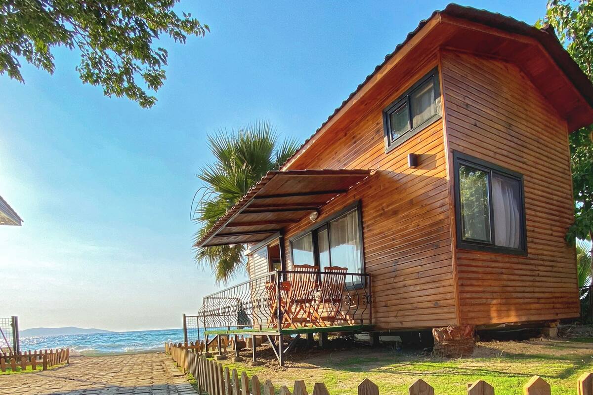 A wooden cabin with a balcony, a view of the sea, and a paved pathway leading to the beach.