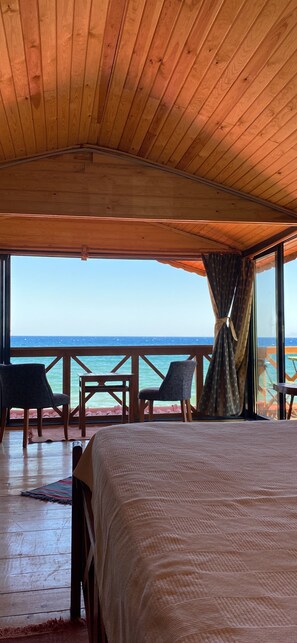 Techo de madera, una cama, una mesa y sillas en una habitación con vista al océano.