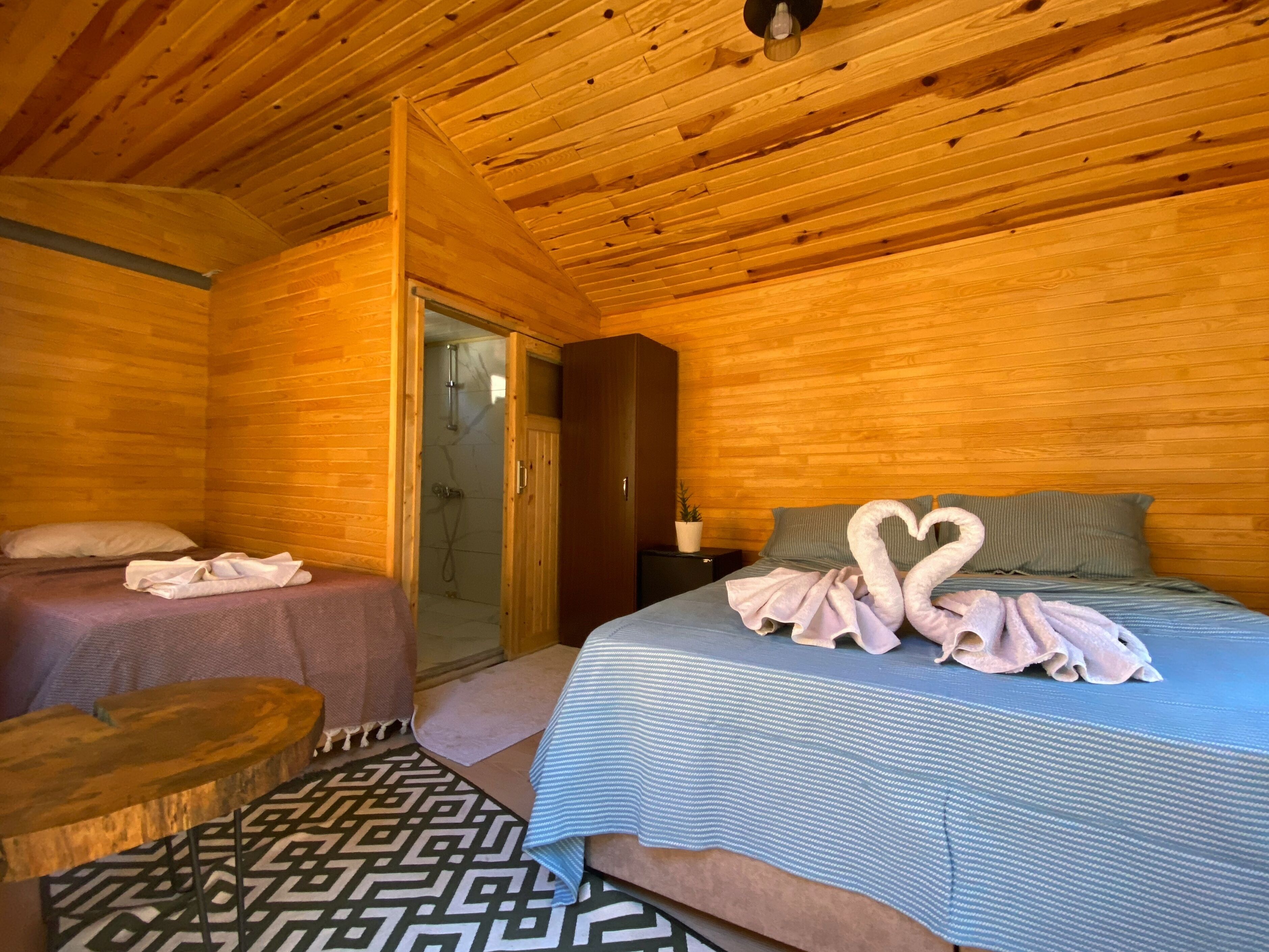 A wooden cabin room with a bed, two pillows, a small table, and a shower area.