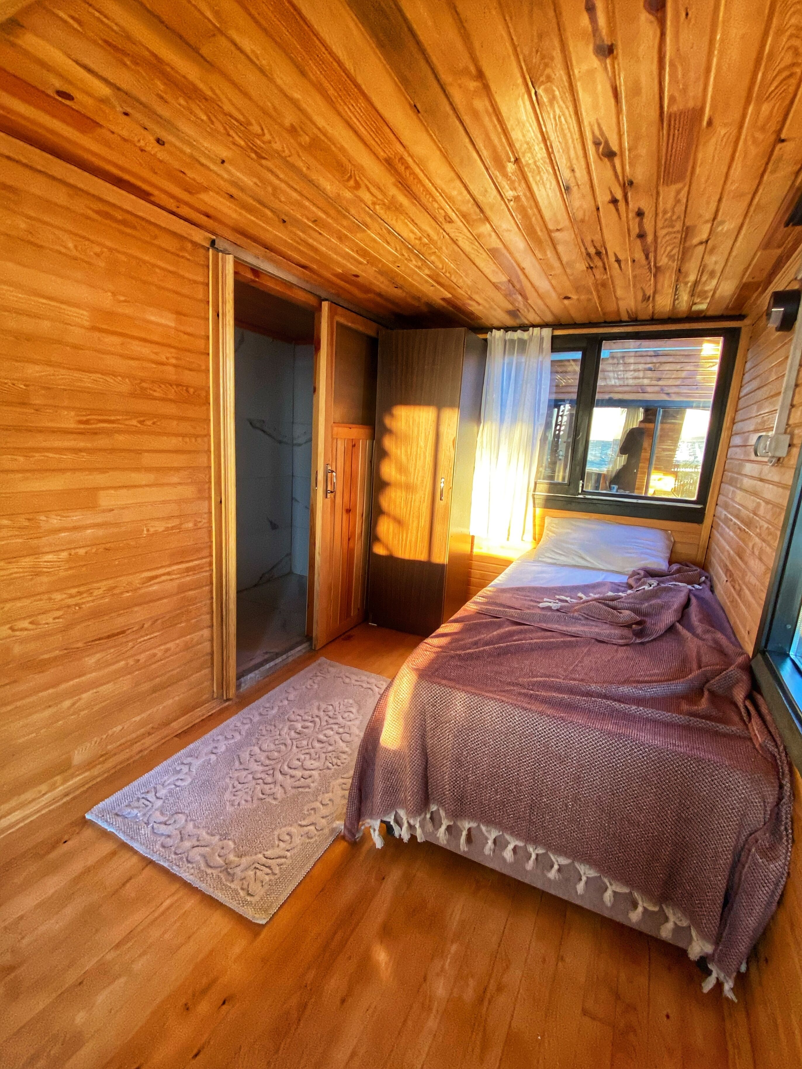 A wooden cabin room with a bed, a door, and a window.