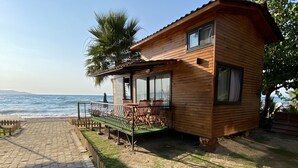 Una cabaña de madera con balcón que da al mar, un sendero pavimentado y una zona ajardinada.
