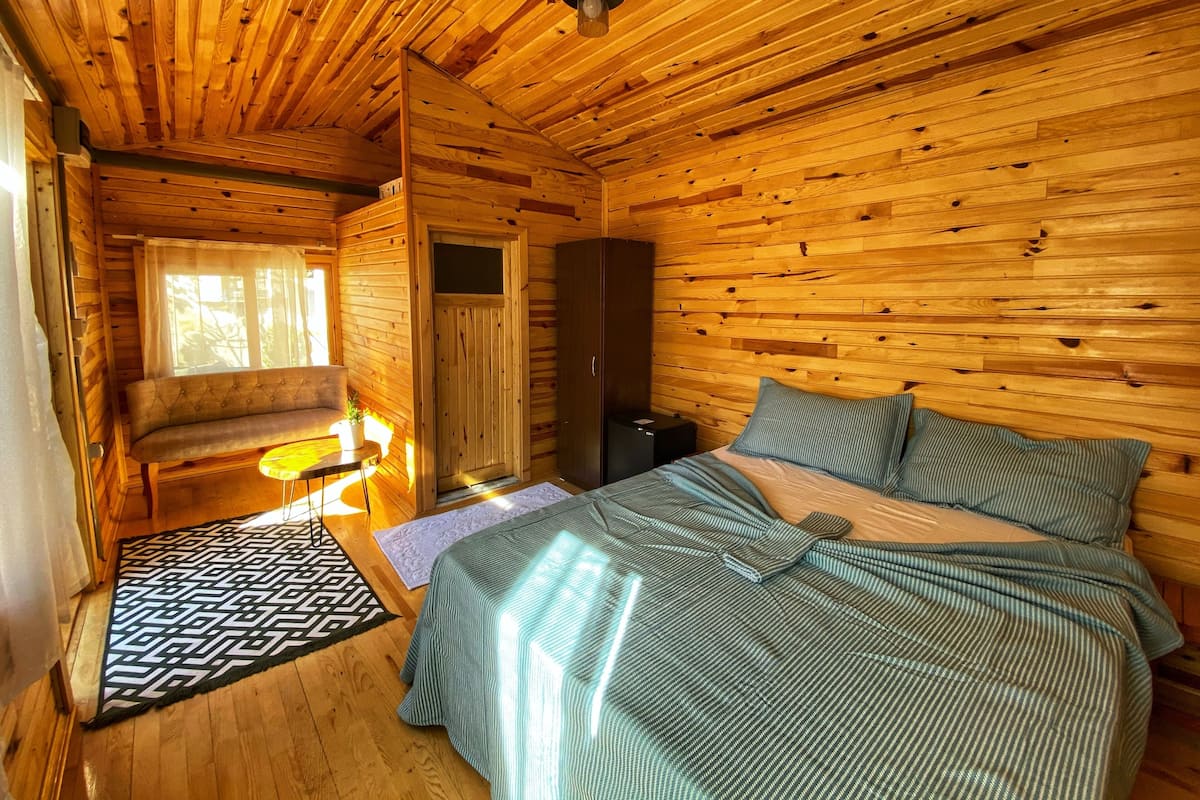 A wooden cabin room with a bed, a bench, a small table, and a door.