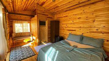 Una habitación de cabaña de madera con una cama, un banco, una mesita y una puerta.