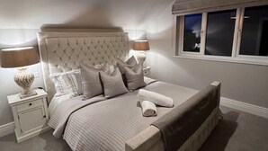 A bedroom with a large bed, a nightstand, a lamp, and a window.