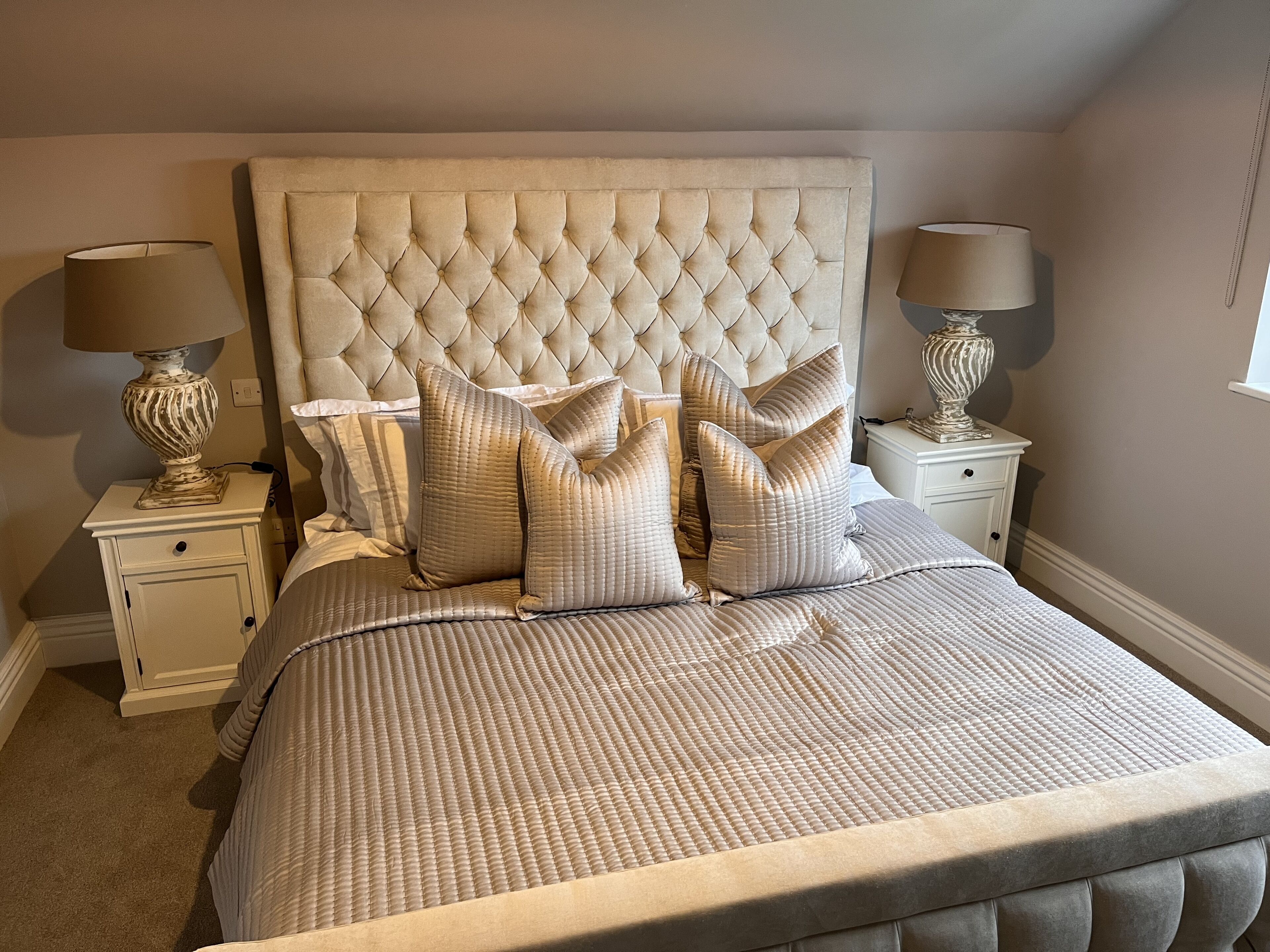 Une chambre à coucher avec une tête de lit capitonnée, un lit recouvert d’une couvre-lit à rayures et deux tables de chevet avec des lampes.