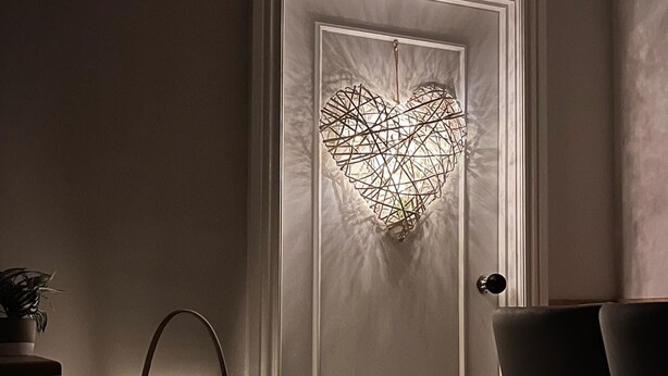A room with a frosted glass door featuring a geometric heart design, a clear glass lantern with candles, and a black chair.
