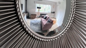 A round mirror with a sunburst frame reflecting a room with a sofa, a window, and a radiator.