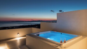 Un jacuzzi en la azotea con vistas a la puesta de sol sobre el agua, dos copas de vino y un diseño arquitectónico moderno.