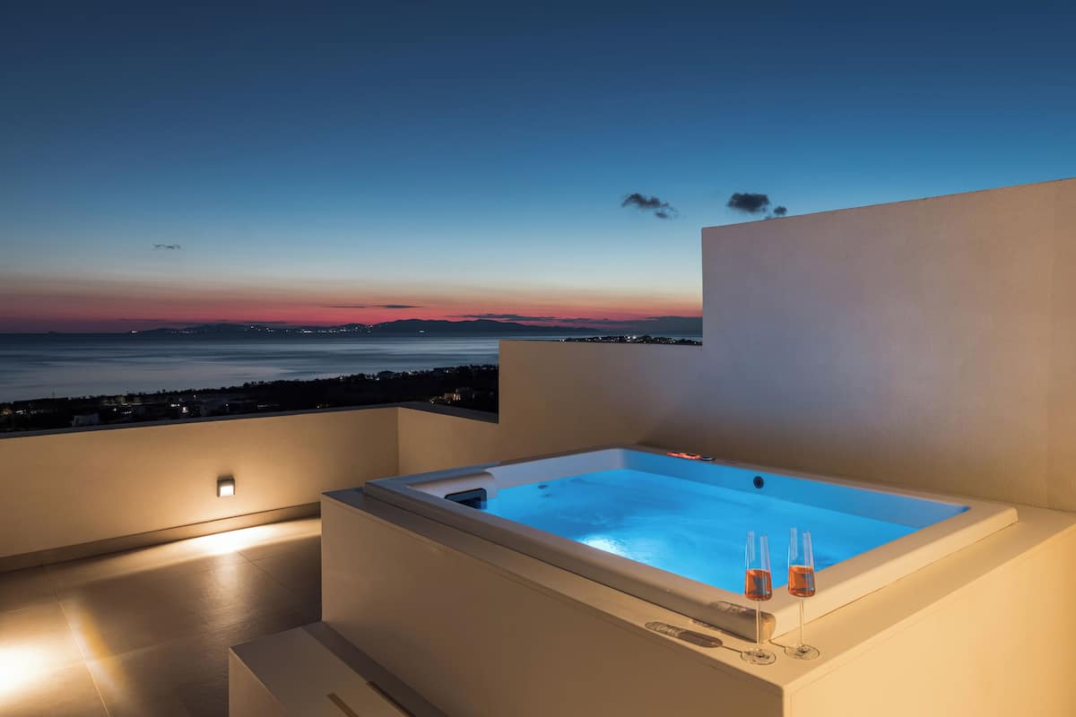 Un jacuzzi en la azotea con vistas a la puesta de sol sobre el agua, dos copas de vino y un diseño arquitectónico moderno.