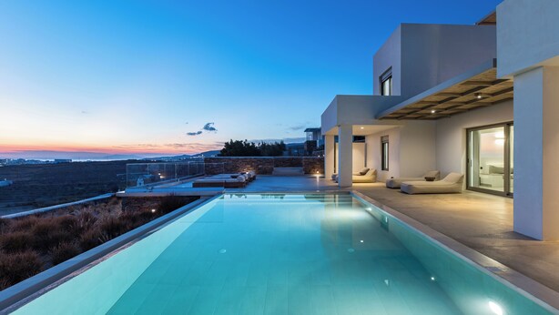 Un área de piscina moderna con una vista despejada del paisaje, un edificio contemporáneo con amplios ventanales y una zona de estar exterior bien iluminada.