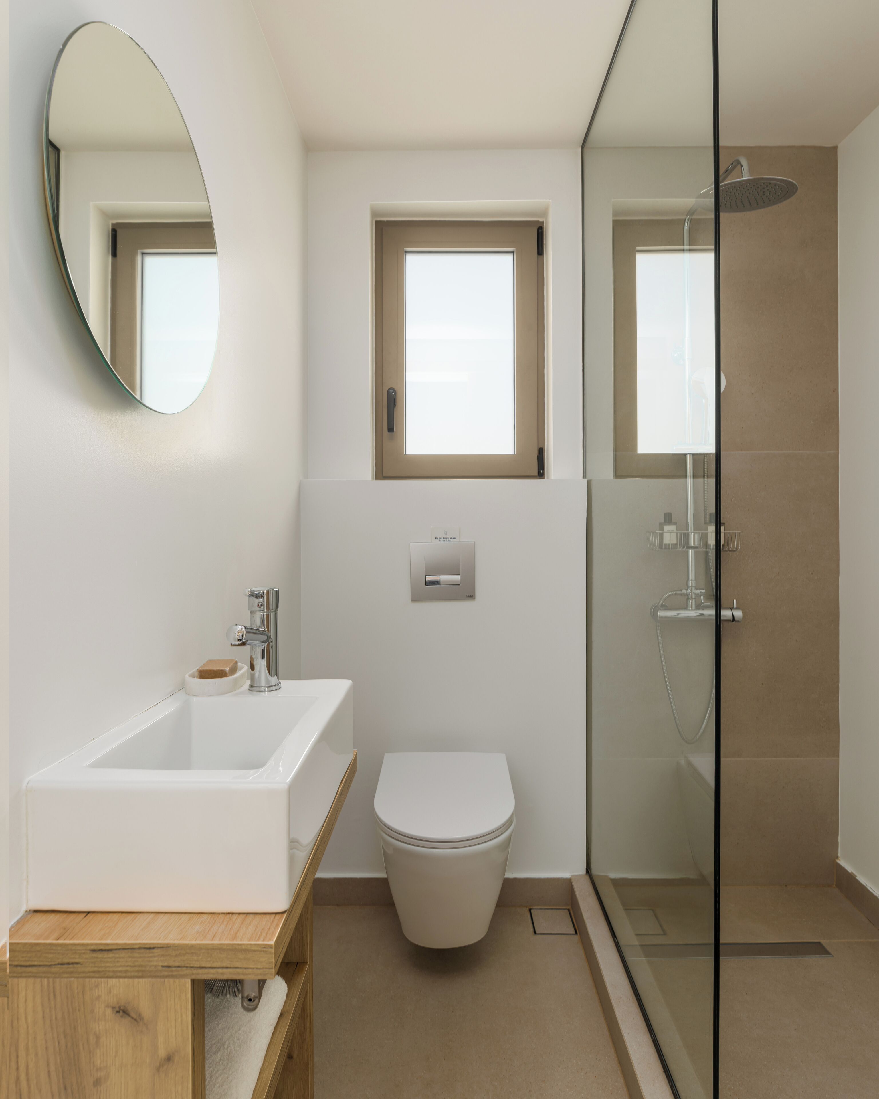 Un baño moderno con un lavabo blanco grande, un inodoro y una zona de ducha con mampara de vidrio.