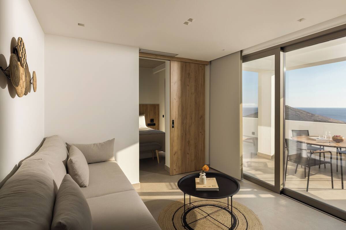 Una sala de estar moderna con un sofá, una mesita y vistas al exterior a través de grandes puertas de vidrio.