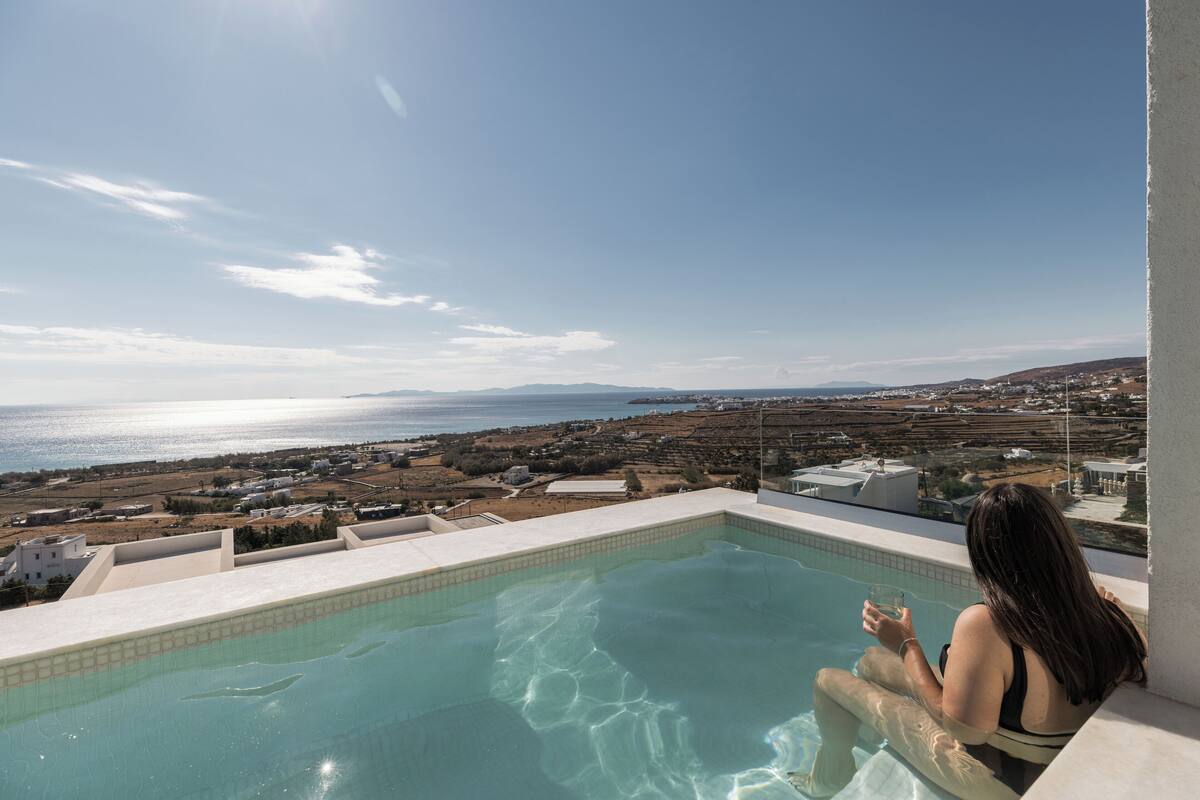 Una mujer descansando junto a una piscina con vistas al mar y al paisaje lejano.