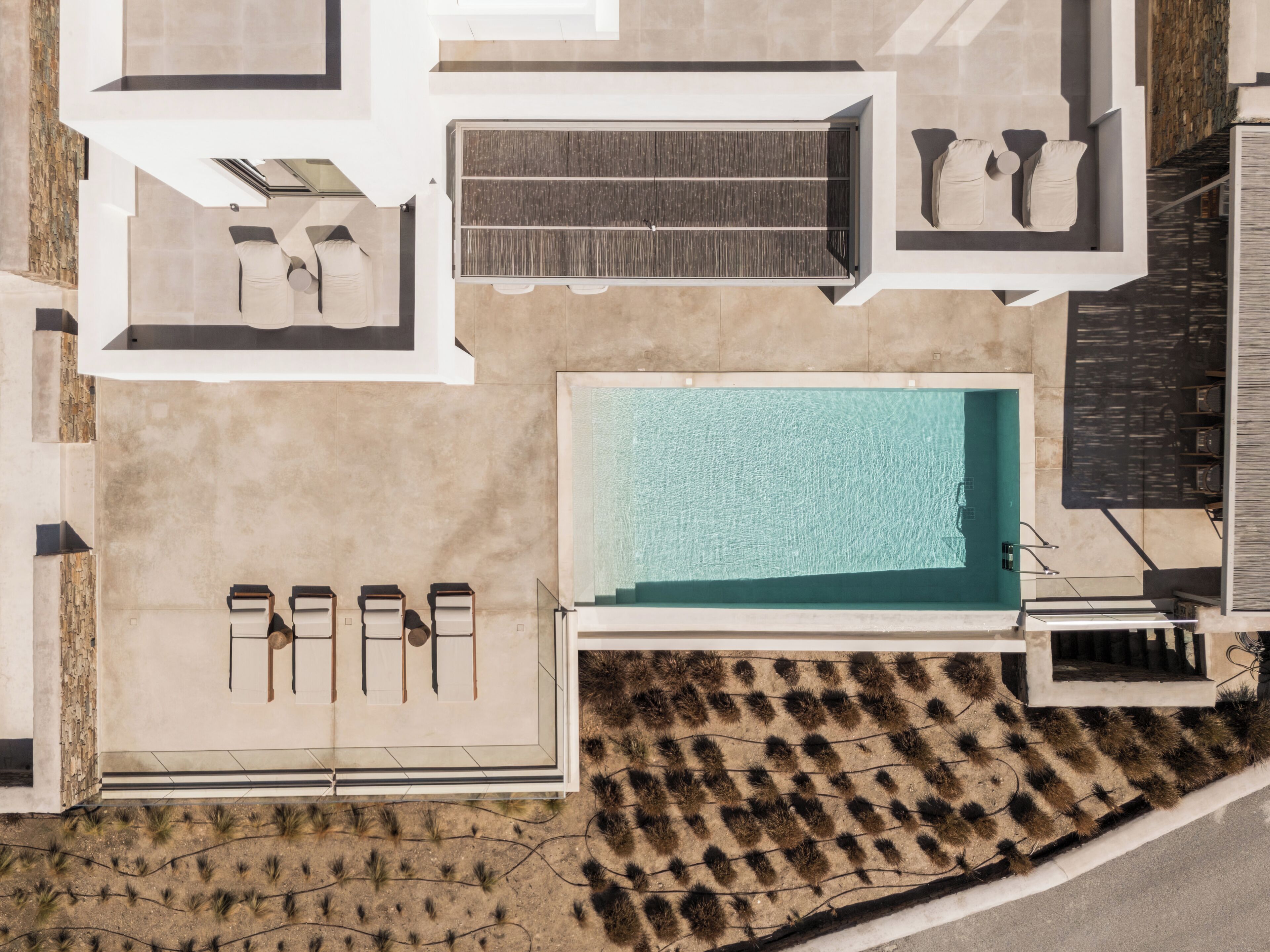 An aerial view of a modern resort with a large swimming pool, sun loungers, and a covered seating area.