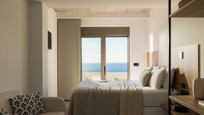 Un dormitorio con cama, sofá y vista al mar a través de un amplio ventanal.