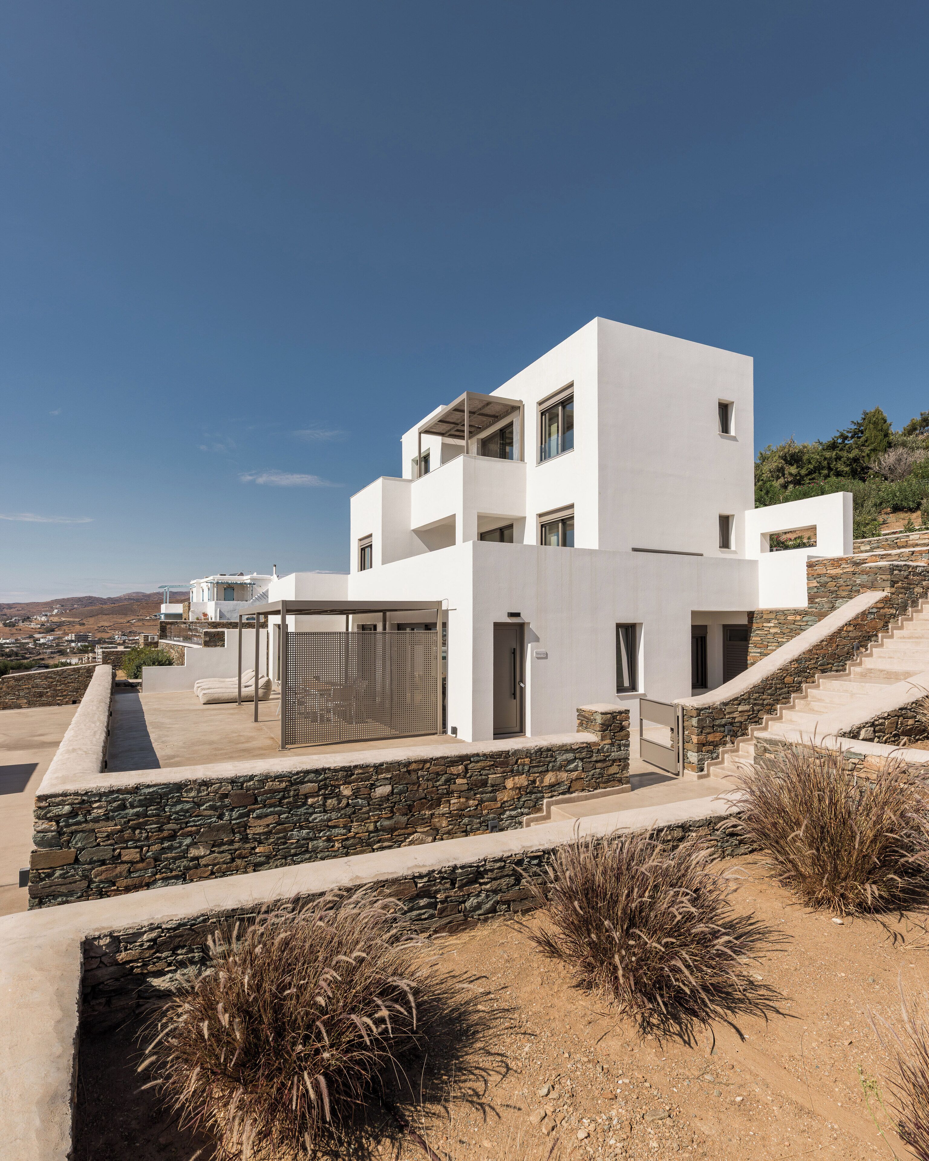Un edificio moderno de varios pisos con un muro de contención de piedra, un área de estar al aire libre cubierta y vistas del paisaje circundante.