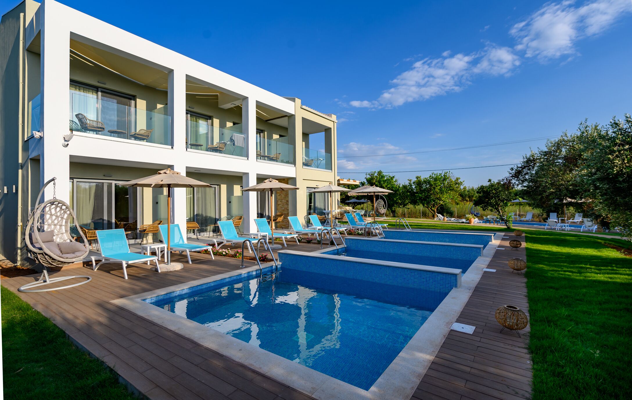 Un edificio moderno de dos pisos con piscina, mobiliario exterior y un césped bien cuidado.