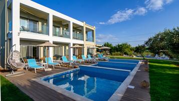 Un edificio moderno de dos pisos con piscina, mobiliario exterior y un césped bien cuidado.