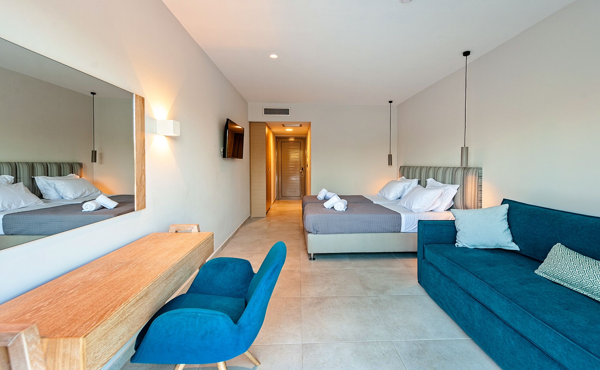 A hotel room with two beds, a desk, a chair, and a sofa.