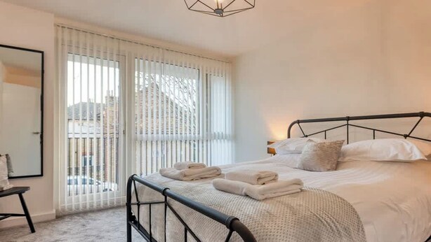 A bedroom with a bed, a window with blinds, a bedside table, and a hanging light fixture.