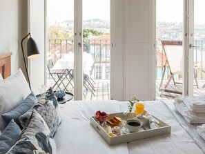 A hotel room with a bed, a tray with breakfast items, a view of the city, and a balcony with a table and chairs. - Down2Town Guest House (Porto)
