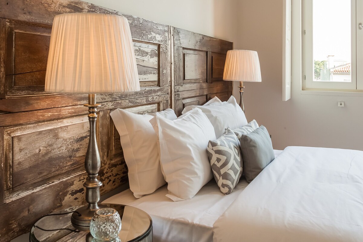 A neatly made bed with white and patterned pillows, a wooden headboard, and two bedside lamps.