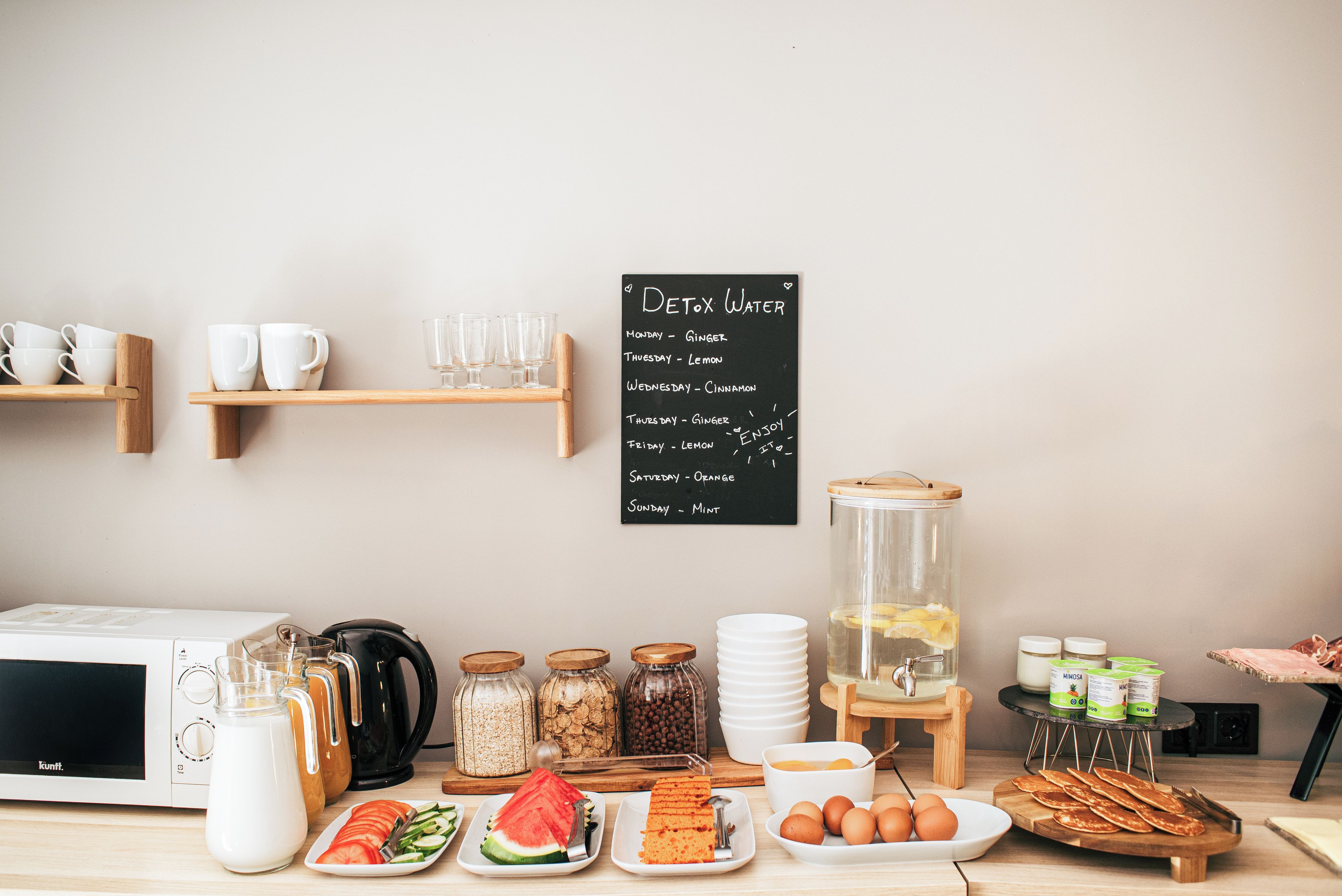 Disposição para o café da manhã, incluindo um quadro de menu, cafeteira, jarra de leite, cereais e diversas opções de alimentos.