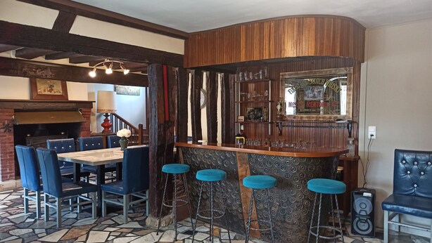 A bar area with a wooden counter, stools, and a seating area with chairs and a table. - Vacation home for 10 people 1h15 from Paris (Venon)