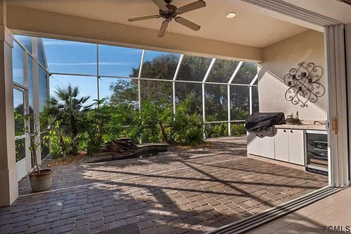Un patio amplio con suelo de ladrillo, ventanas de vidrio grandes y un ventilador de techo.