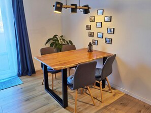 A dining area with a wooden table, four chairs, a potted plant, and wall-mounted picture frames.