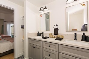 Un baño moderno con un espejo grande, dos luces empotradas, un perchero y un lavamanos con artículos de aseo.