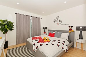 Un dormitorio moderno con una cama, dos mesitas de noche, un adhesivo de pared de Mickey Mouse y una planta en maceta.