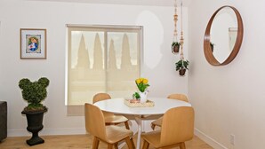 Ein Essbereich mit einem runden Tisch, vier Stühlen, einer Zimmerpflanze und einem Fenster mit Blick auf Bäume.