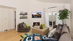 Ein modernes Wohnzimmer mit Kamin, Flachbildfernseher und Bücherregal mit Kinderbüchern.