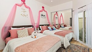 Ein Hotelzimmer mit zwei Betten, jeweils mit rosa Bettwäsche und einem Baldachin. Auf einem Bett liegen Zierkissen und ein Plüschtier. Das Zimmer verfügt über einen großen Spiegel und ein Fenster mit Vorhängen.