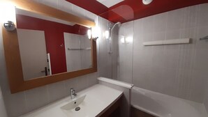 Casa de banho com lavatório branco, um espelho grande, chuveiro e uma parede com detalhes vermelhos.
