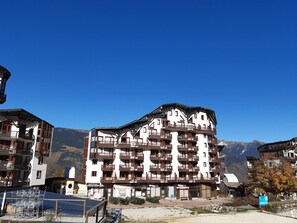 A multi-story hotel with balconies, a ski resort sign, and mountains in the background. - Spacious apartment 5 pax, south-facing balcony, parking included (La Tania)