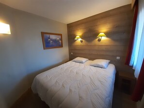 A hotel room with a wooden headboard, two wall-mounted lamps, a bed with white bedding, and a framed picture on the wall.