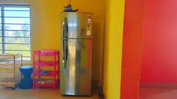 A stainless steel refrigerator in a room with yellow and orange walls, a window with blinds, and a blue trash bin.