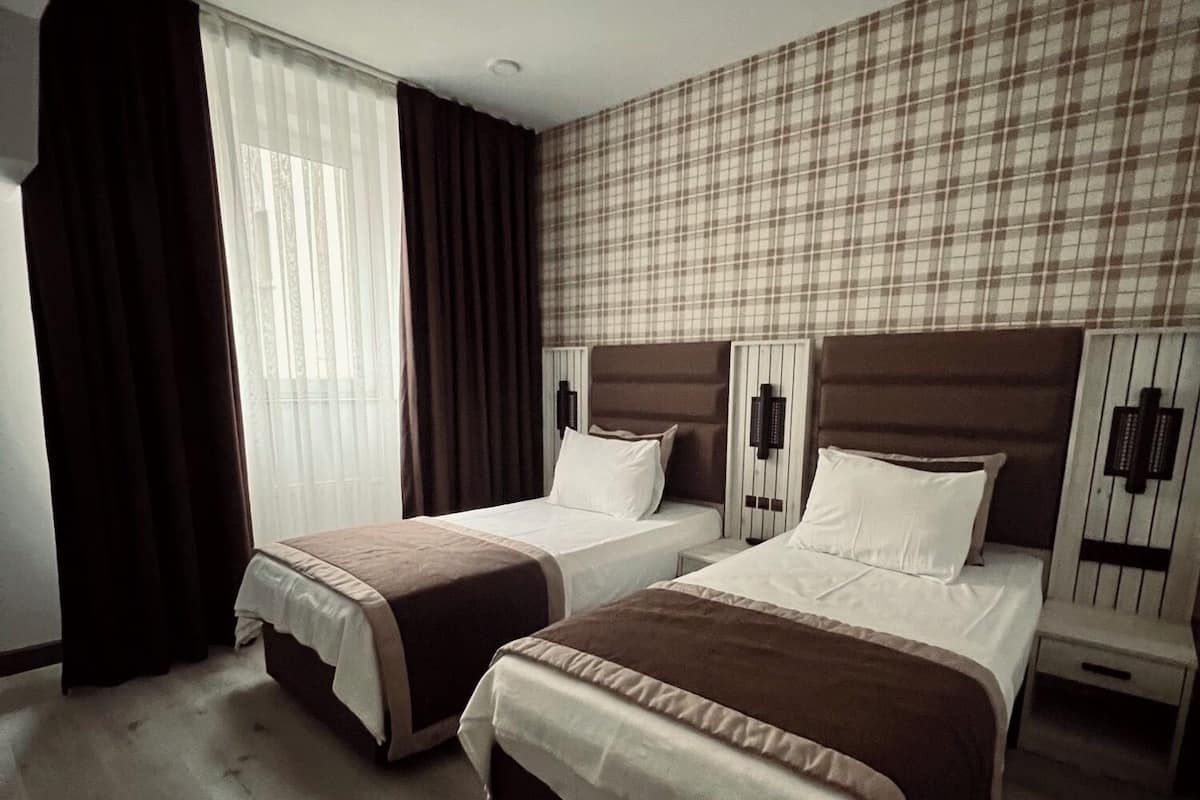 Ein Hotelzimmer mit zwei Betten, einem großen Fenster mit Vorhängen, einer Wand mit Karomuster und einem Holzboden.