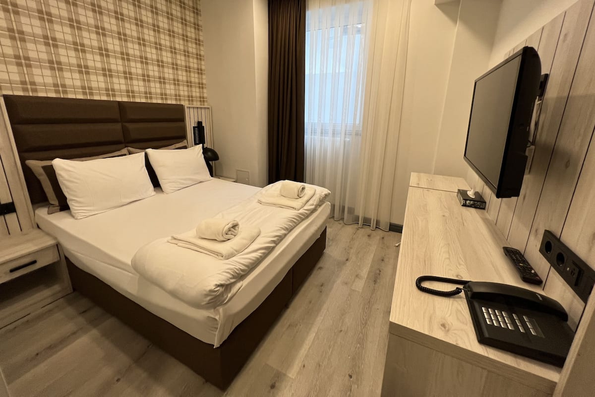 Ein Hotelzimmer mit Bett, Fernseher, Telefon und einem Fenster mit Vorhängen.