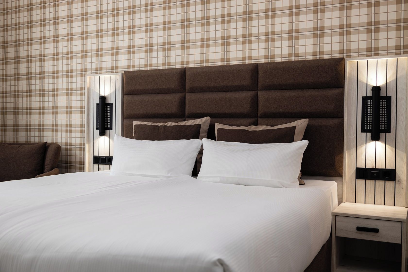 A hotel room with a large bed, a headboard, two bedside tables with lamps, and a plaid-patterned wall.