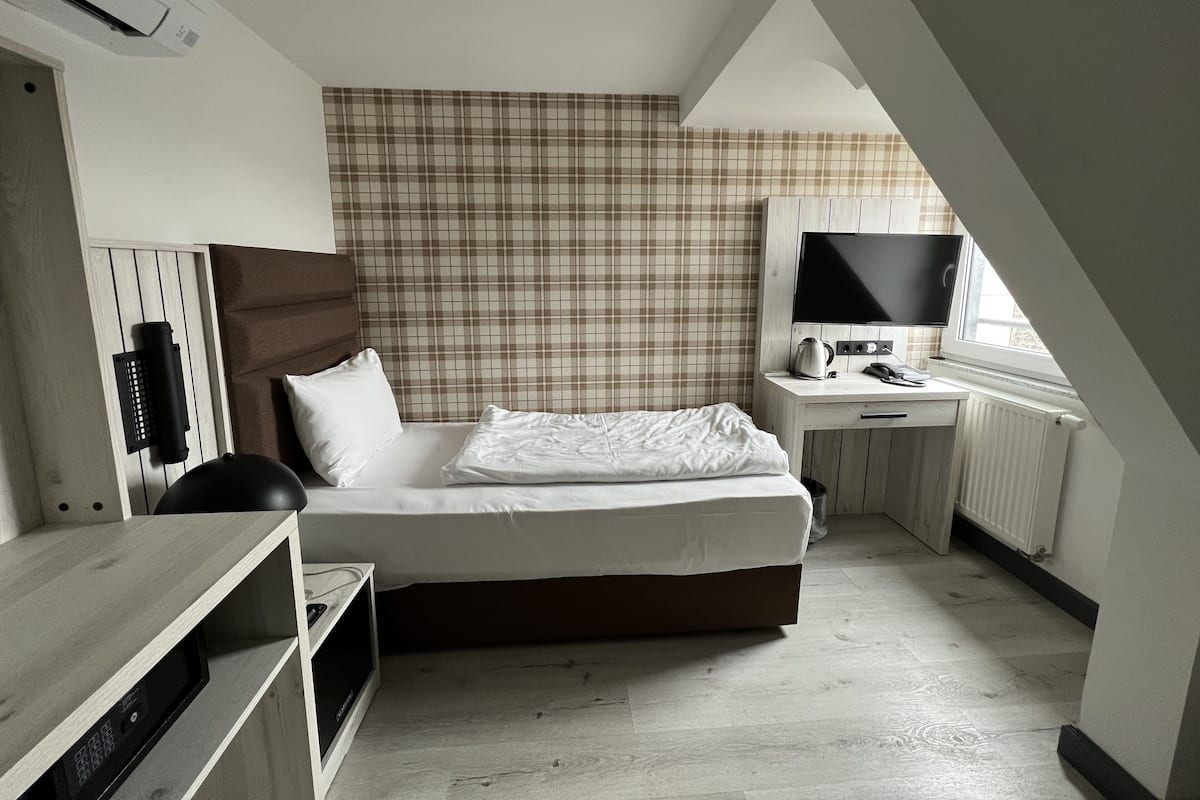 Ein Schlafzimmer mit einem Bett, einem Schreibtisch mit Computer, einem Fernseher und einer Heizung.