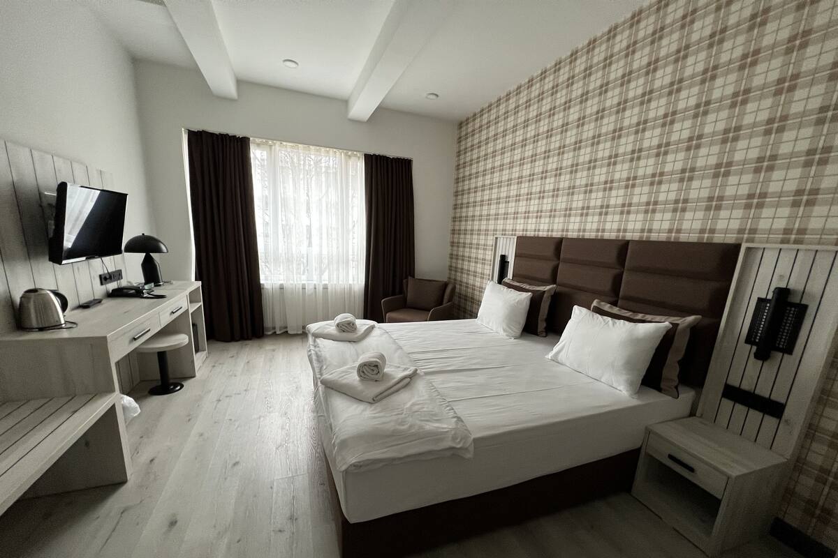 Ein Hotelzimmer mit einem großen Bett, einem Schreibtisch mit Computer, einem Sessel und einem Fernseher.