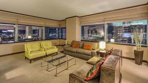 A modern hotel room with a large window offering a city view, a green sofa, a grey sofa, and a small table. - Biggest Penthouse at Vdara! 2 BR Stunning 270° Strip Views! Sleeps 7! 42nd Floor (Las Vegas)