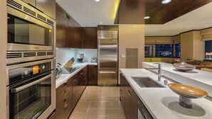 A modern kitchen with stainless steel appliances, a central island with a sink, and a view of the city at night. - Biggest Penthouse at Vdara! 2 BR Stunning 270° Strip Views! Sleeps 7! 42nd Floor (Las Vegas)