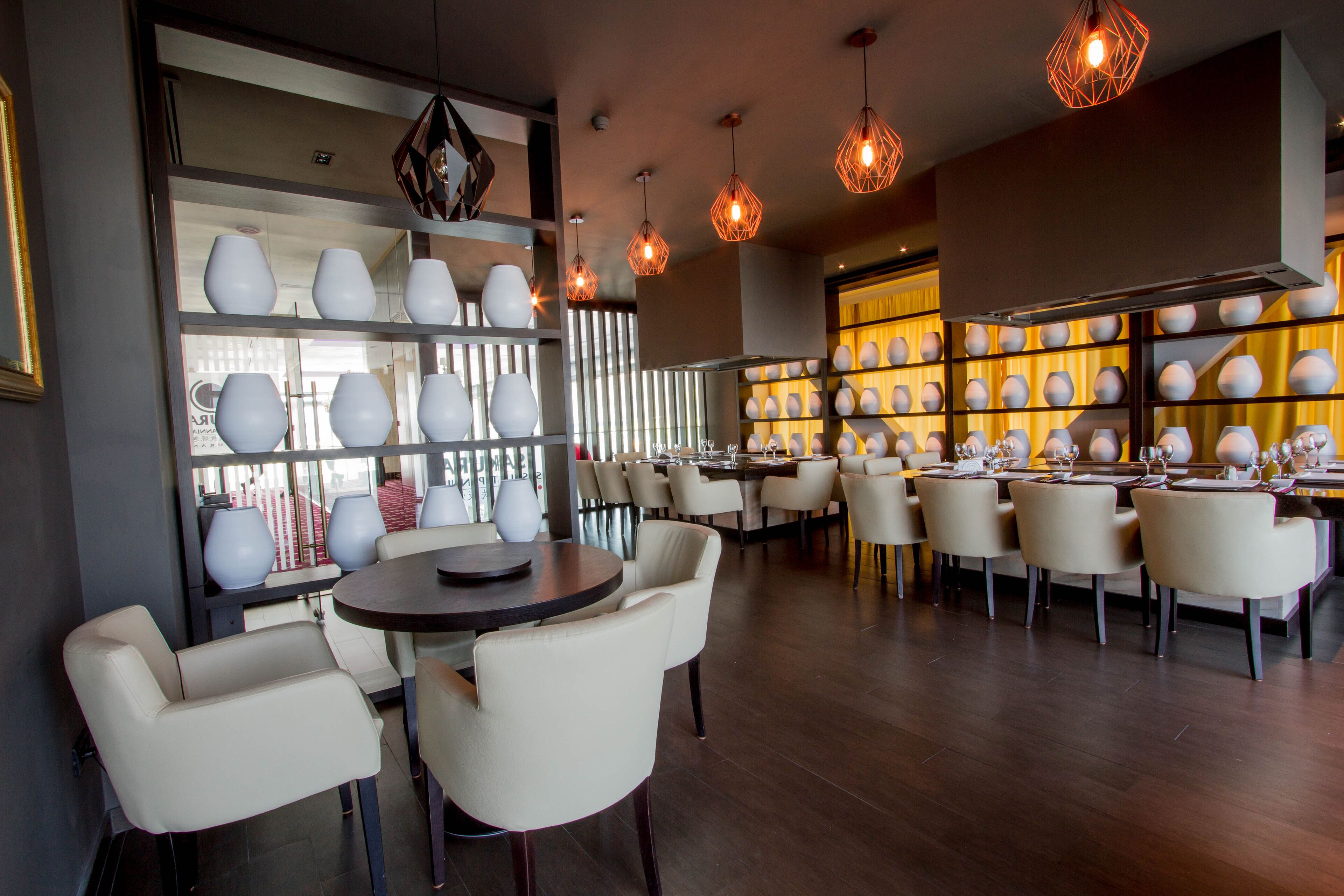 A modern dining area with round tables, white chairs, and decorative vases on shelves.
