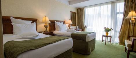 Habitación de hotel con dos camas, alfombra verde, una mesita con un jarrón y una silla.