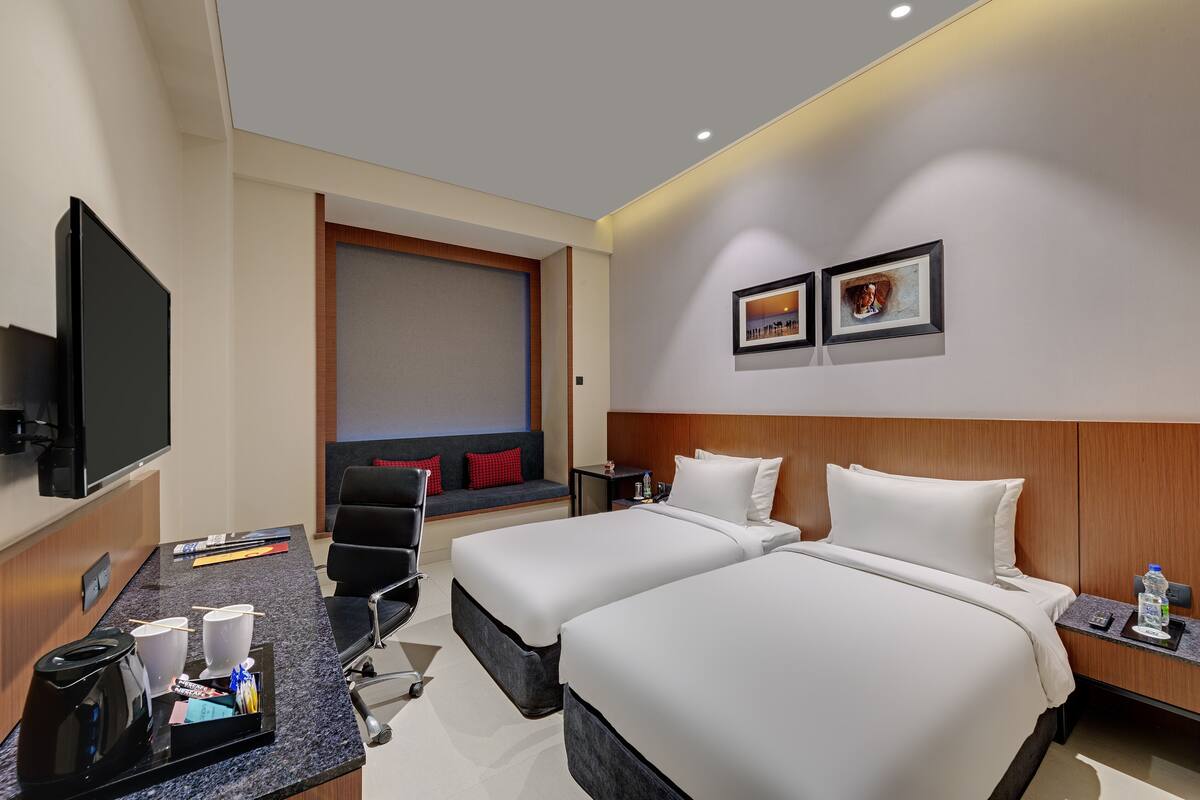 A hotel room with two beds, a desk with a coffee maker, a TV, and artwork on the wall.